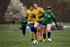 Players in yellow and green jerseys compete intensely for the soccer ball during an outdoor match on a grass field.