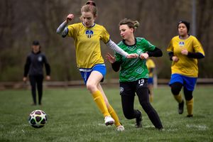 Soccer players compete for the ball during an intense match on a grass field in yellow and green uniforms.