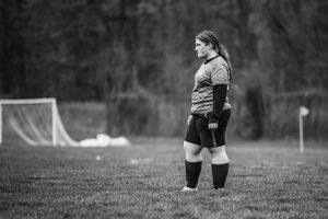 A goalkeeper stands alert on a soccer field in black and white, wearing knee pads and a long sleeve jersey.