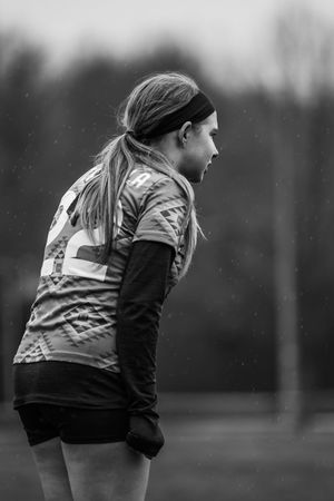 Black and white rugby player in striped jersey stands focused during outdoor match in cold weather.