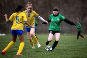 Soccer players in yellow and green jerseys compete for control of the ball during an intense match on a grass field.