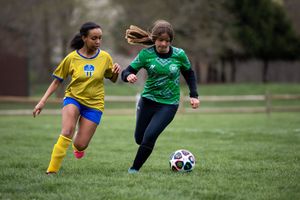 Two soccer players compete for the ball during a match, one in yellow and one in green jerseys on a grass field.