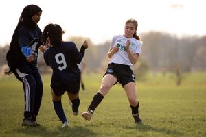 Youth soccer players battle for possession of the ball during an outdoor match on a grass field at sunset.