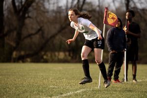 Soccer player in white jersey prepares to make a play while an official with flag observes from the sideline.