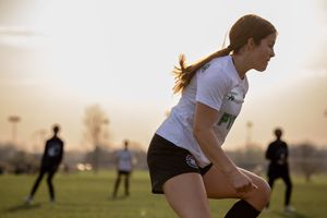 Athletes playing soccer at sunset with silhouettes visible in the golden evening light.