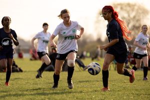 Soccer players compete for the ball during an intense match on a grass field at sunset.