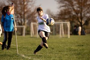 A soccer player dribbles the ball across a grass field while a referee with a flag watches from the sideline.