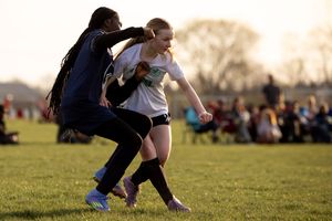 Two athletes compete for possession during an intense soccer match on a grassy field at sunset.