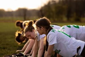 Athletes warming up and stretching on a sports field during golden hour sunset training session.