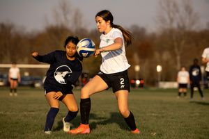 Two soccer players compete for control of the ball during a late afternoon match on a grass field.