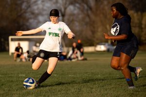 Two soccer players compete for the ball during a match on a grass field in evening sunlight.