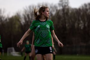 Soccer player in green jersey and black shorts makes a dynamic play during an outdoor match in cloudy weather.