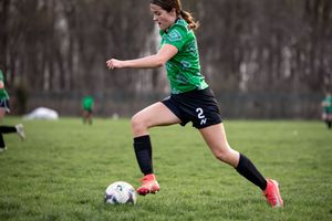 Soccer player in green jersey dribbles ball during training session on grass field in overcast weather.