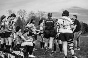 A women's rugby team huddles together on a field during practice in black and white photography.