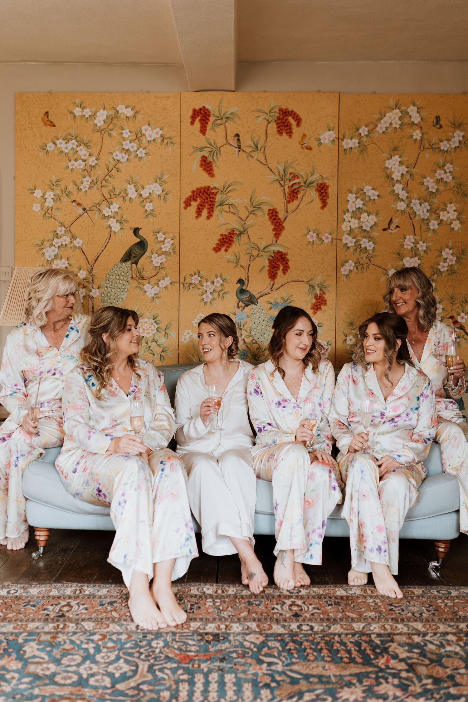 A group wearing matching floral robes lounges together against an ornate gold folding screen with cherry blossoms.