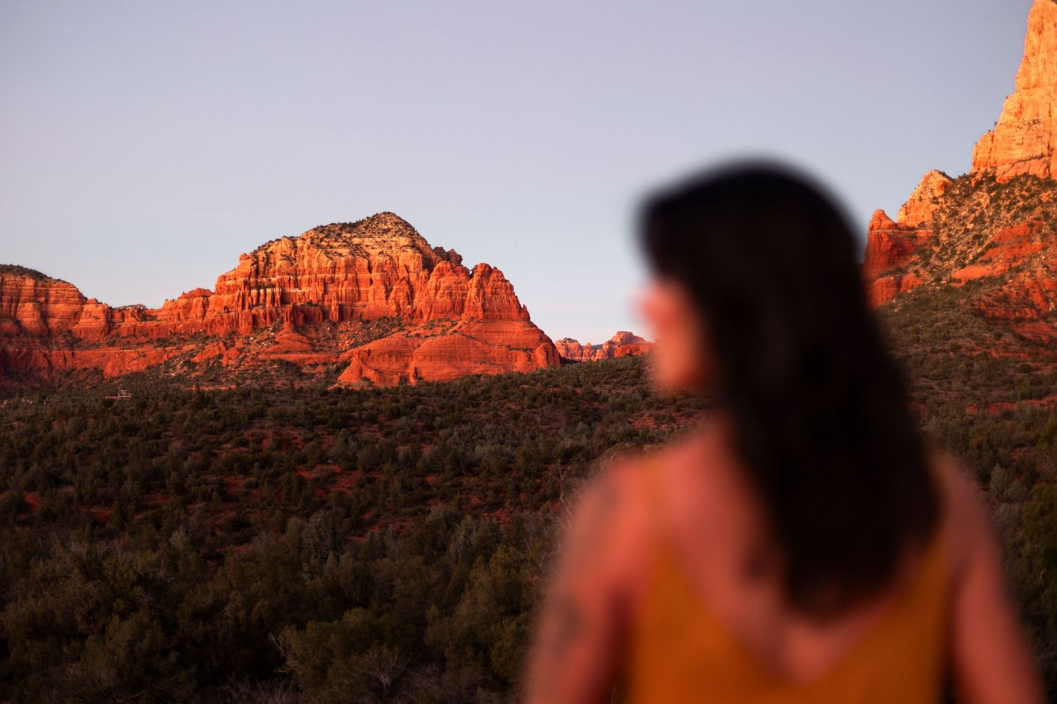Woman in yellow top gazing at red rock formations in Sedona Arizona at golden hour.