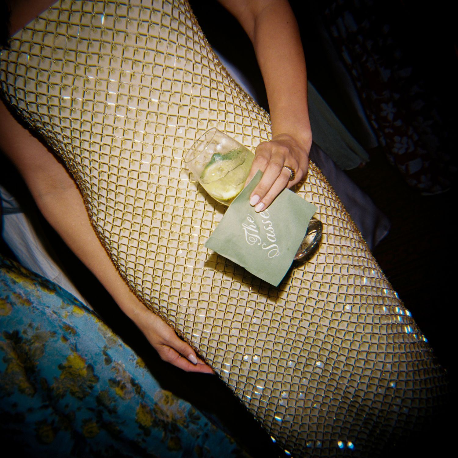 Woman in gold sequin dress holding a cocktail with lime garnish at a formal evening event.