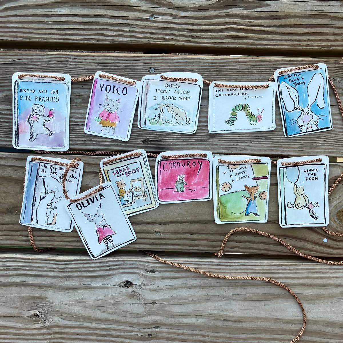 A hand-painted garland featuring miniature illustrated covers of beloved children's books like "Corduroy," strung together with twine
