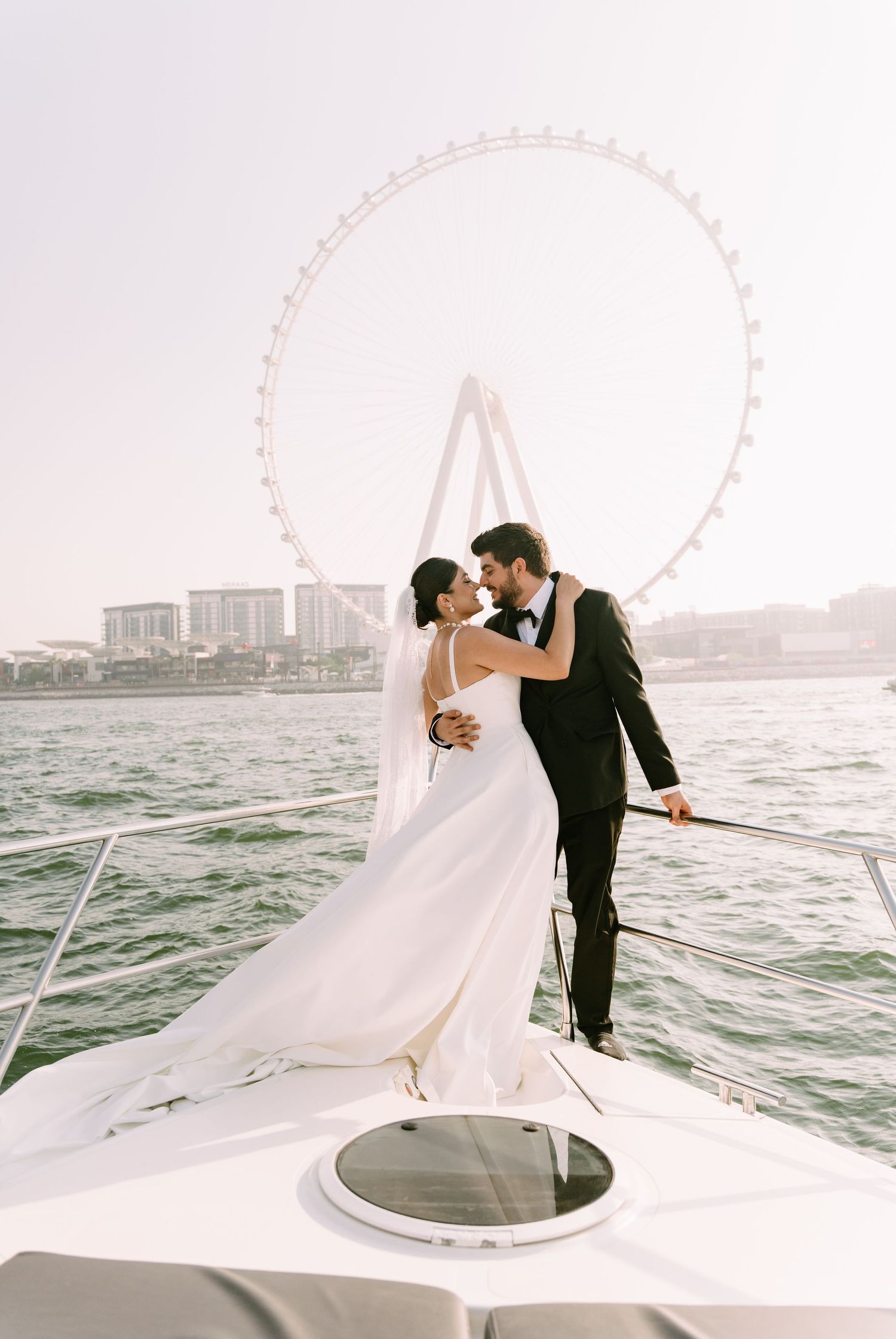 A romantic wedding couple embraces on a yacht with the London Eye visible in the background across the Thames River.