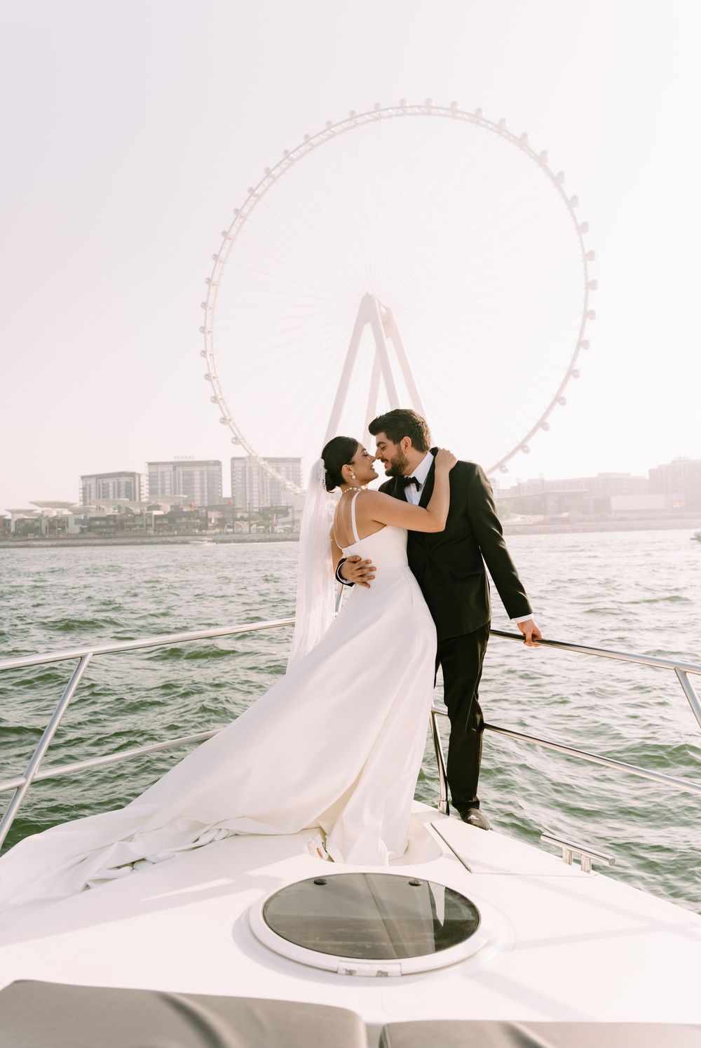 A romantic wedding couple embraces on a yacht with the London Eye visible in the background across the Thames River.