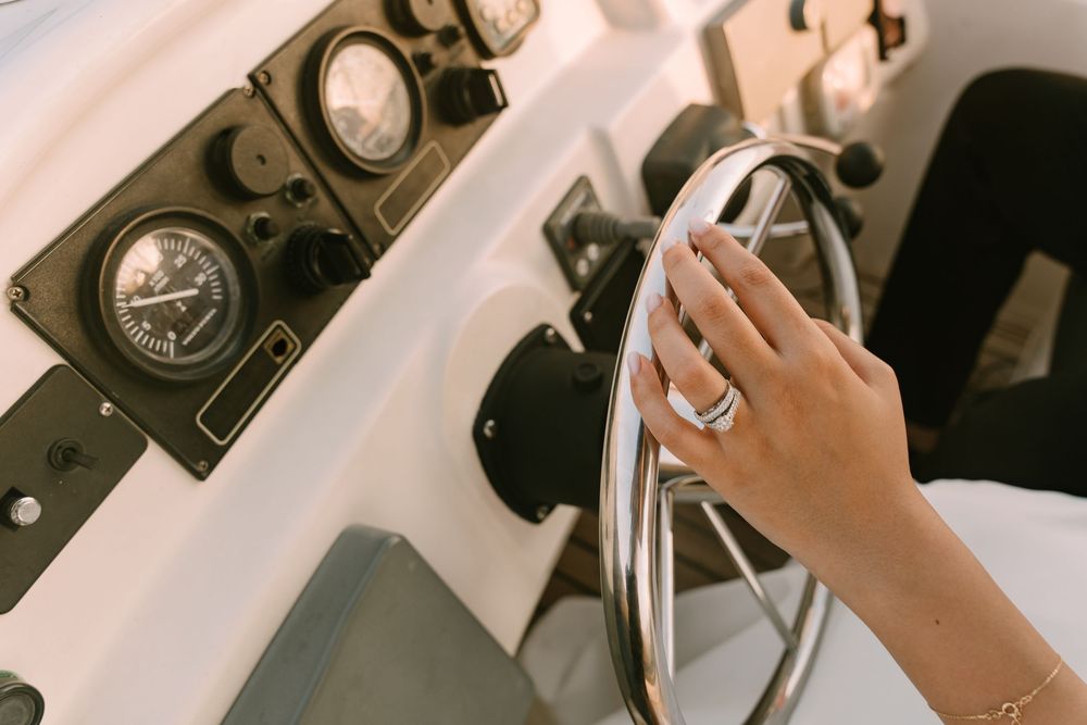 Close-up view of a hand steering a boat wheel with vintage nautical gauges visible in the background.