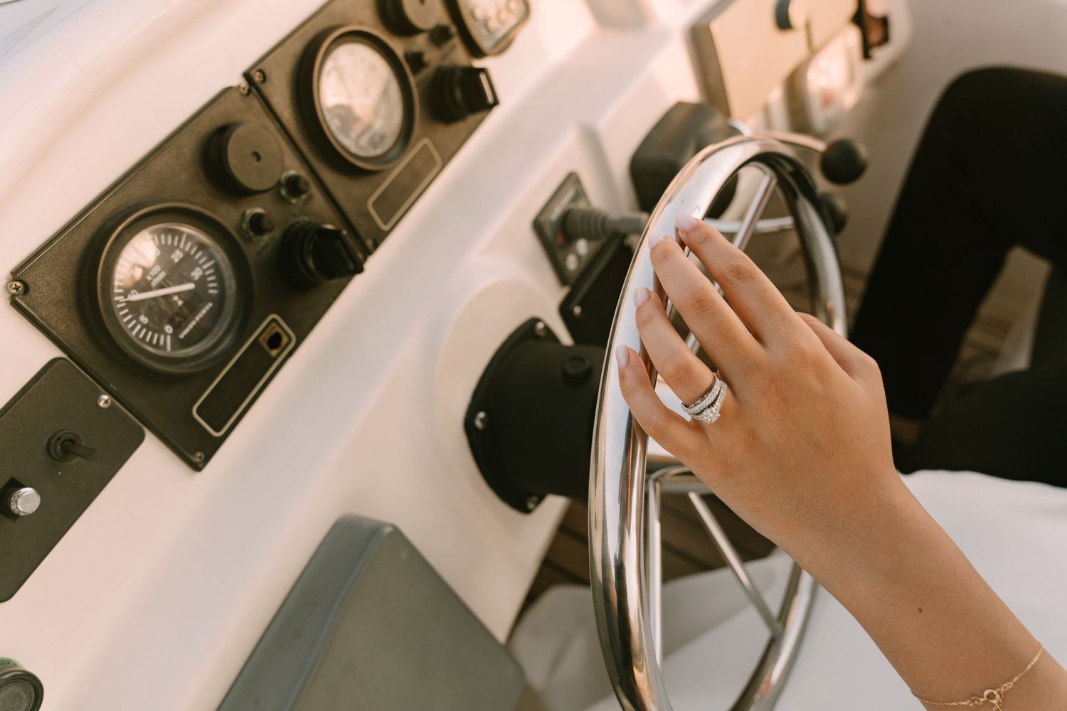 Close-up view of a hand steering a boat wheel with vintage nautical gauges visible in the background.