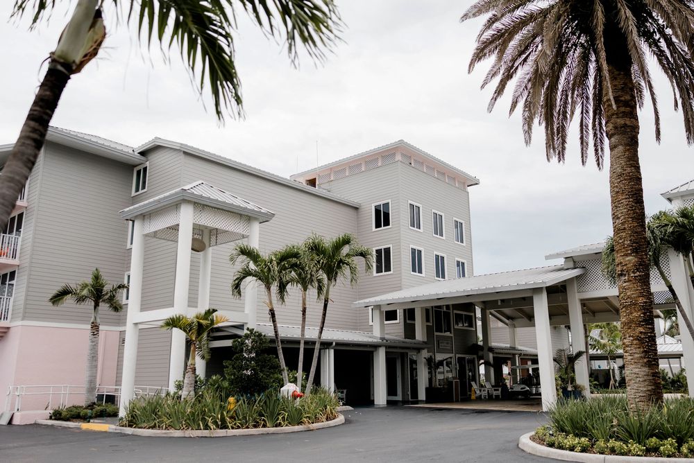 White coastal hotel building with palm trees and covered entrance driveway in Florida.