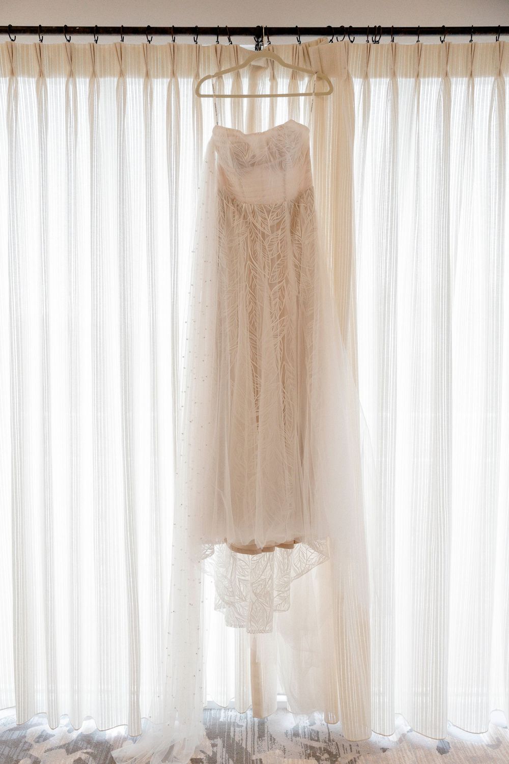 White vintage-style wedding dresses displayed hanging in a row against sheer curtained windows with natural light.