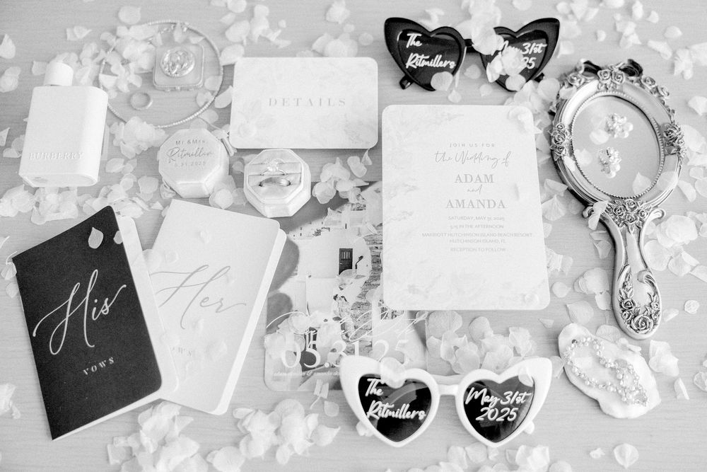 Wedding accessories and stationery arranged in black and white with invitations, mirror and sunglasses on lace background.