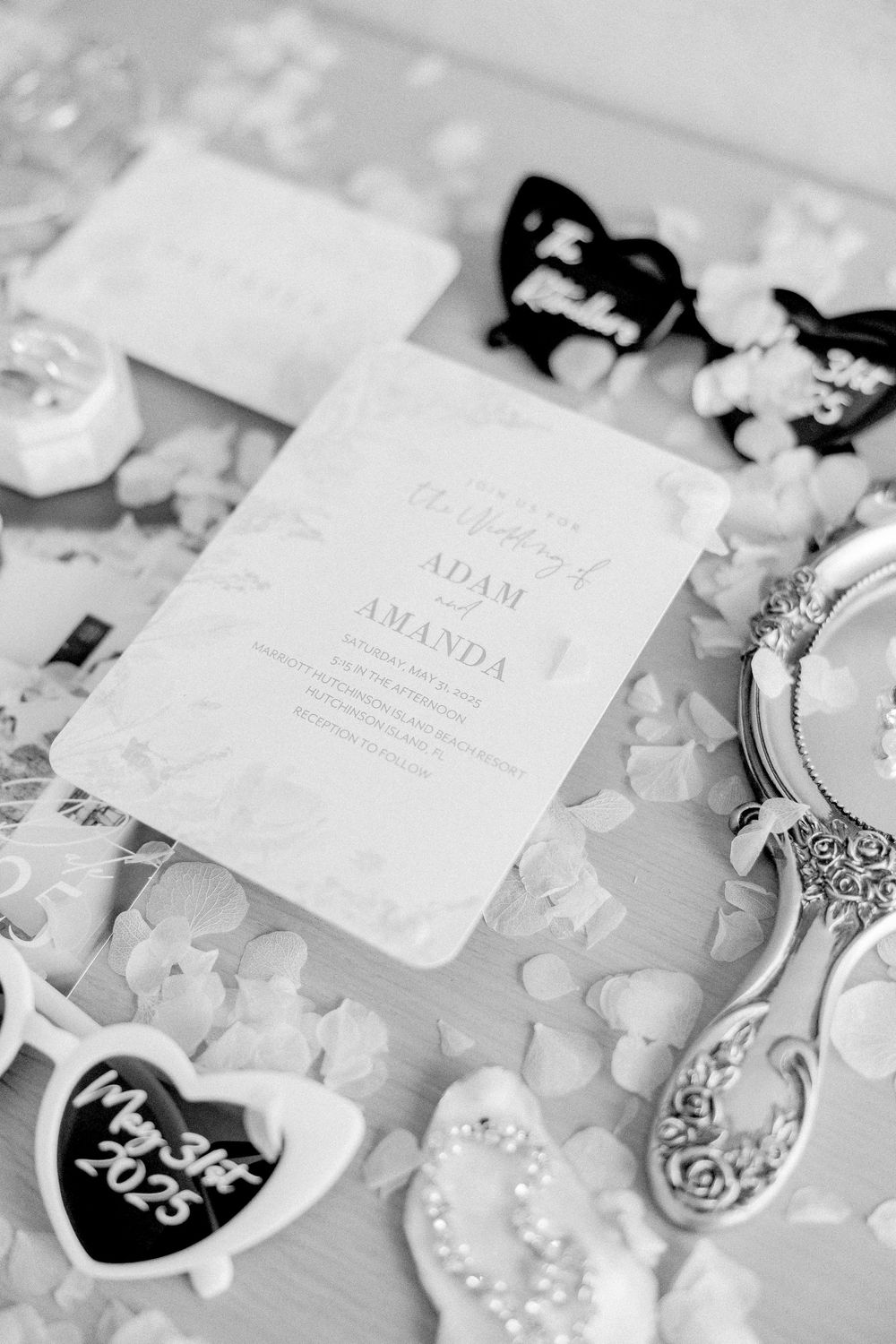 Black and white wedding details including an invitation, decorative hearts, and vintage silverware on a lace tablecloth.