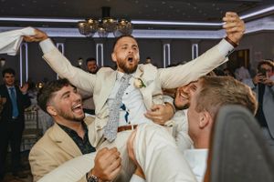 A joyful celebration at a wedding reception as guests lift someone up in celebration amid laughter and excitement.