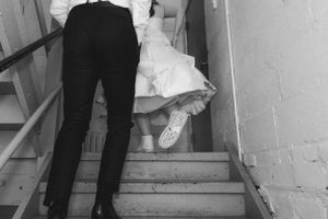Black and white photo showing dress shoes and formal wear on stone stairs, capturing a candid wedding moment.