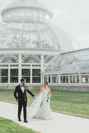 A couple in wedding attire poses outside the elegant glass conservatory at the New York Botanical Garden.