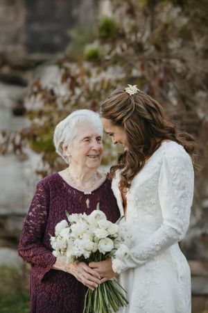 A touching moment between two generations holding a bouquet of white roses in elegant burgundy and ivory lace dresses.
