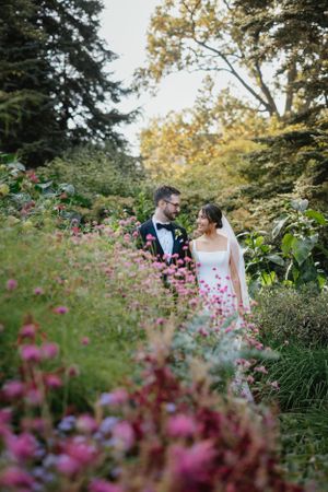 A couple shares a romantic moment among blooming pink wildflowers in a lush garden setting at sunset.