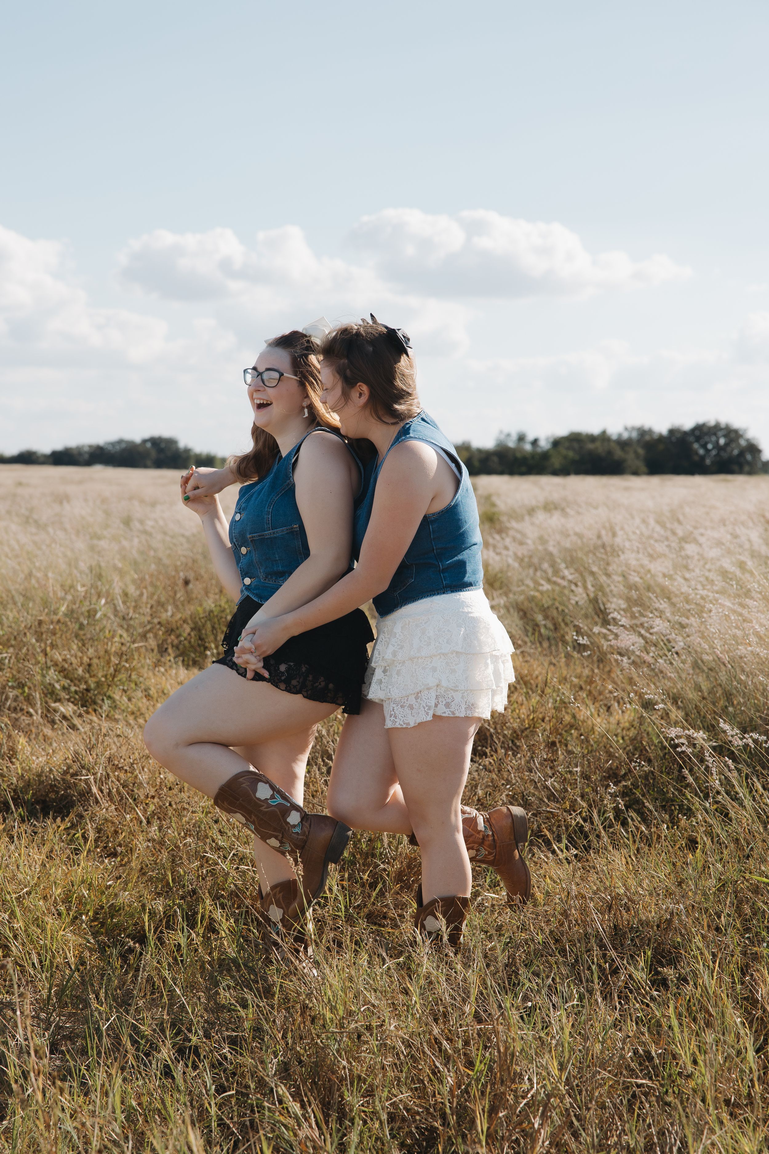 Two friends in matching denim tops posing playfully in sunny wheat field.