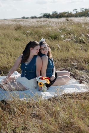 Friends having picnic on blanket in rustic field with sunflowers.