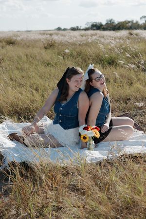 Two friends sharing laughs during outdoor picnic in tall grass field.