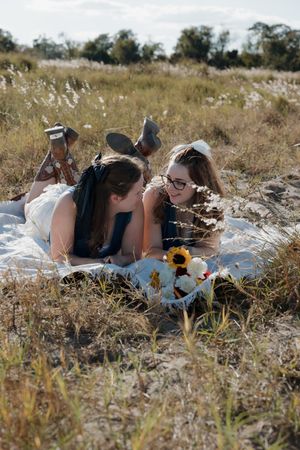 Two people lying in a sunny meadow surrounded by tall grass and wildflowers.