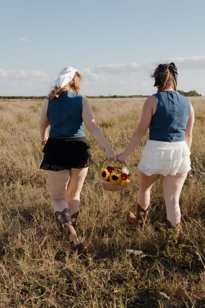 People walking through a golden field at sunset holding sunflowers and wearing matching outfits.