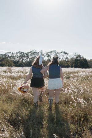 Friends walking together through a sunlit meadow with tall grass and trees in the background.