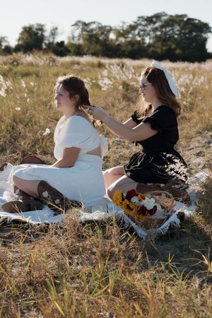 People relaxing on a white blanket in a grassy field with sunflowers nearby.