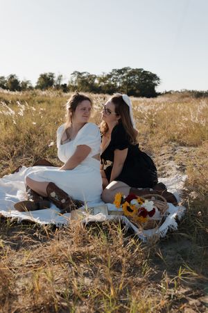 People relaxing in a sun-drenched field with flowers and a white picnic blanket.