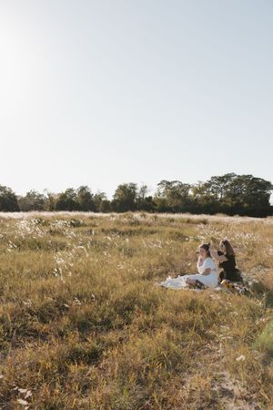 Wide landscape shot of people relaxing in a golden meadow during sunset.