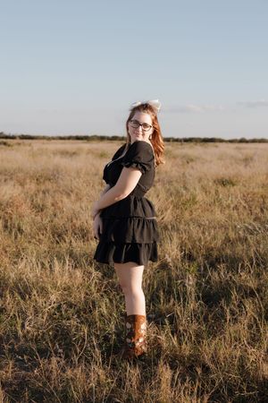 Person in black dress standing in golden field during sunset.