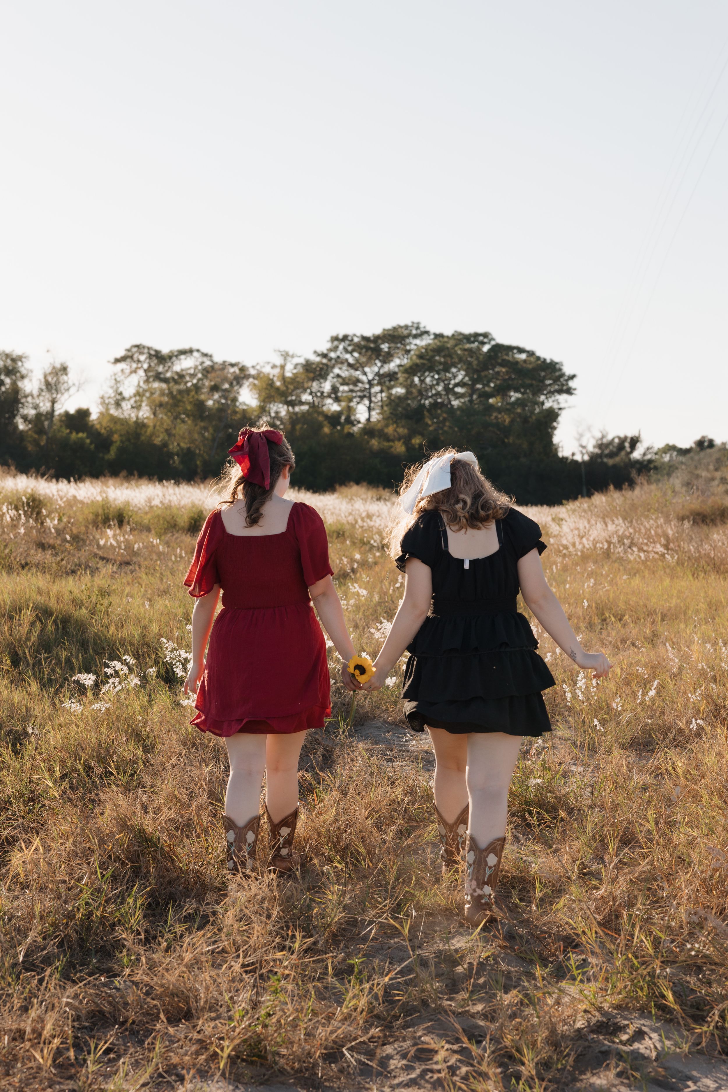Two people walking through tall grass in dresses during sunset.