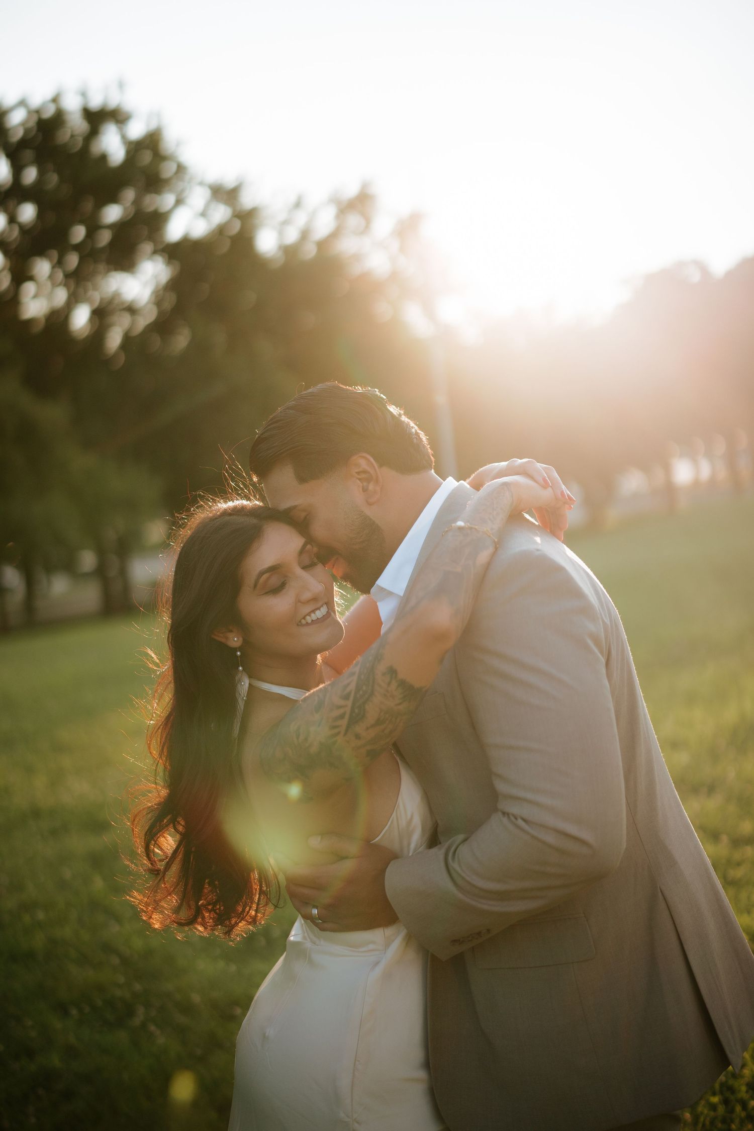 Romantic South Asian engagement photo in a sunlit forest setting, featuring a stylish couple in natural light and elegant attire.