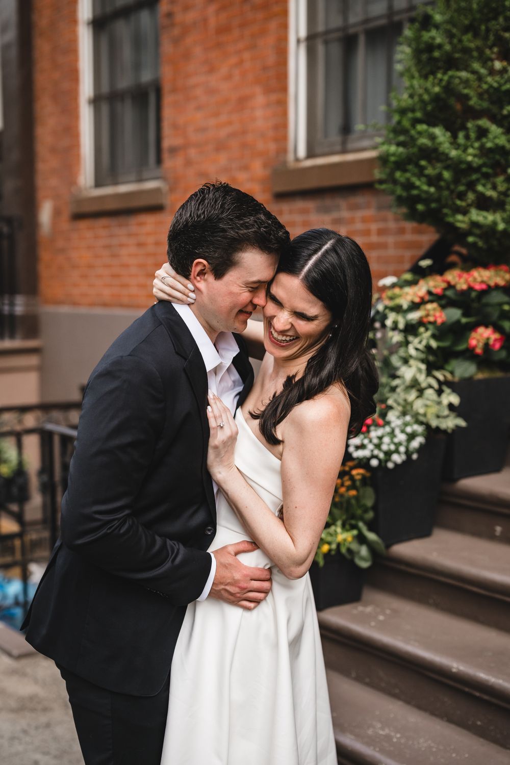 A romantic couple shares an intimate moment on brownstone steps with flowers in the background.