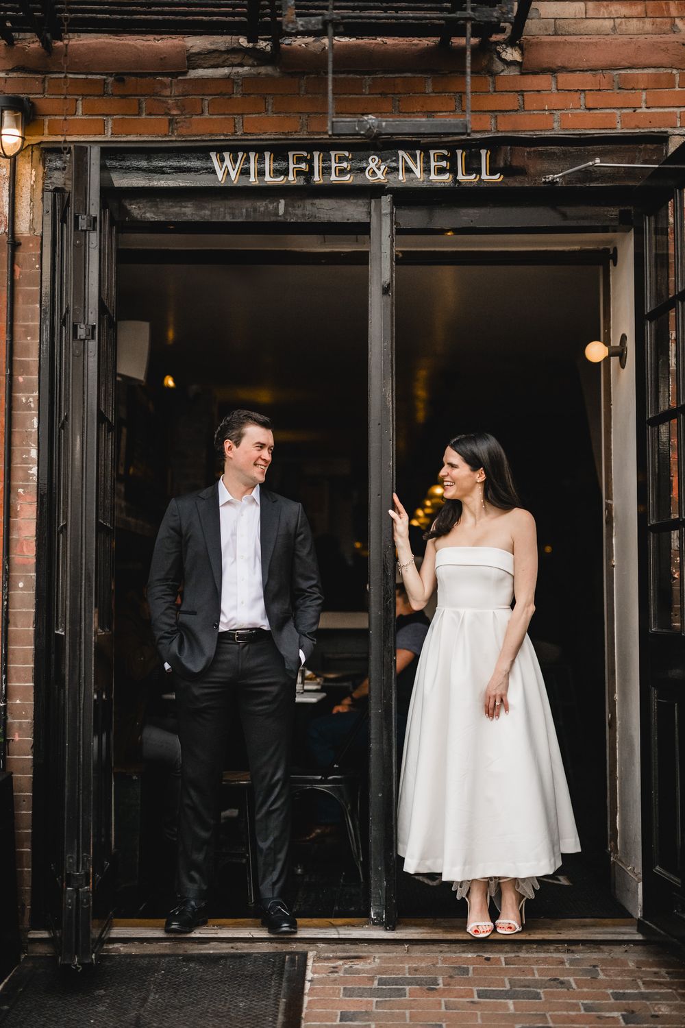 Stylish couple poses in doorway of Wilfie & Nell restaurant against industrial brick facade.