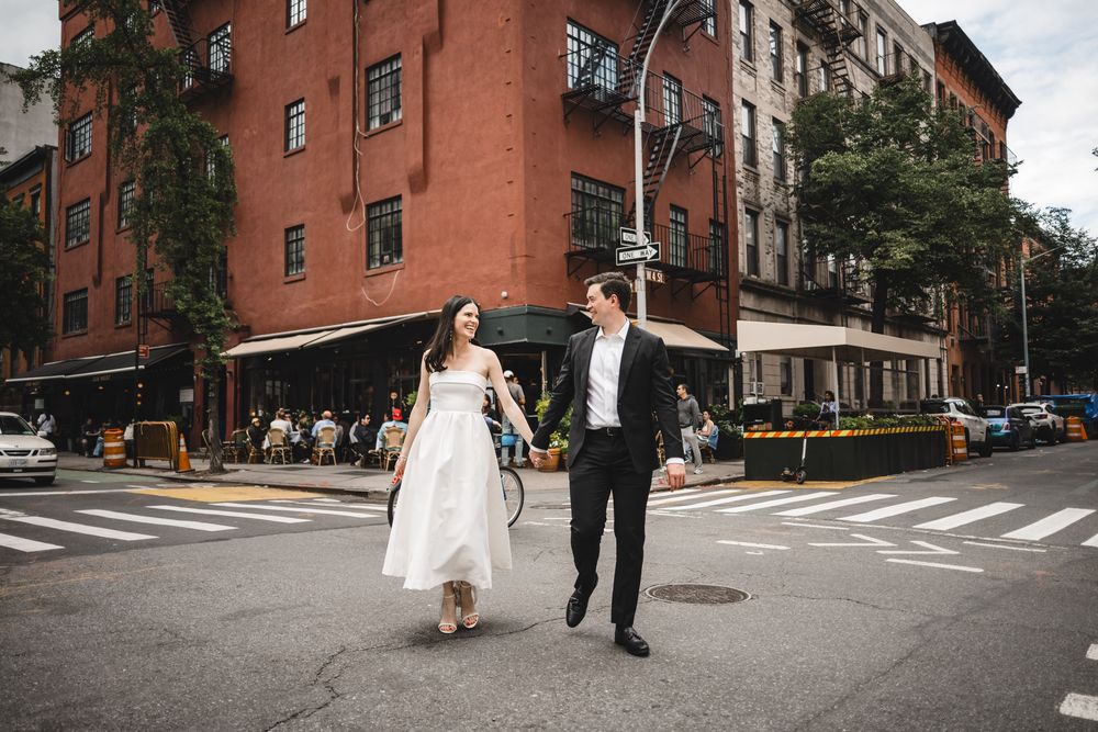 Couple walks hand in hand through urban street intersection in wedding attire.